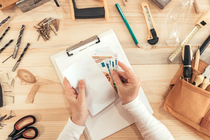 Atelier artisanal avec artisan manipulant billets euros sur plans techniques