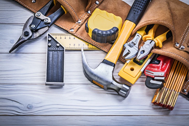 Atelier d'artisan avec ceinture à outils en cuir marron contenant divers outils de construction et menuiserie disposés sur planches de bois clair